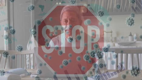 Animation-of-stop-sign-and-virus-cells-over-sad-biracial-man-using-laptop-at-home