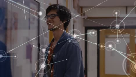 Animation-of-network-of-connections-with-icons-over-happy-caucasian-male-student-in-school