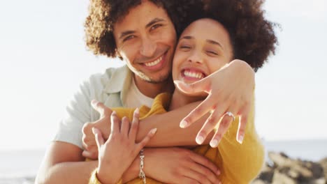 Portrait-of-african-american-couple-smiling-and-showing-their-ring-on-the-rocks-near-the-sea