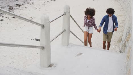 African-american-couple-holding-hands-climbing-up-the-stairs-near-the-beach