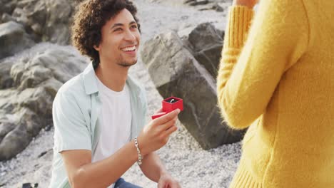 African-american-man-proposing-his-girlfriend-with-a-ring-on-the-rocks-near-the-sea