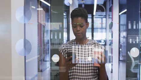 Statistical-data-processing-against-african-american-woman-using-smartphone-while-walking-at-office