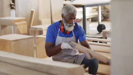 African-american-male-carpenter-looking-and-choosing-wooden-plank-in-a-carpentry-shop