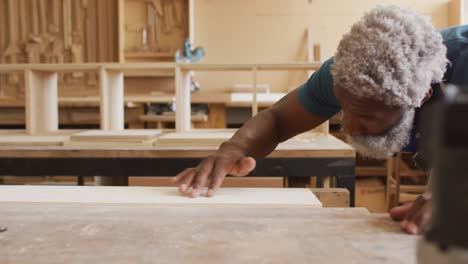 African-american-male-carpenter-blowing-the-dust-over-wooden-plank-at-a-carpentry-shop
