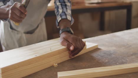 Mittelteil-Eines-Afroamerikanischen-Zimmermanns,-Der-In-Einer-Tischlerei-Nägel-In-Das-Holz-Hämmert