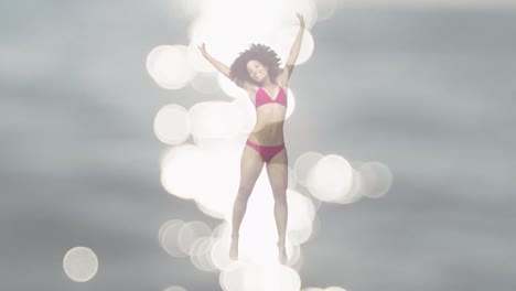 Animation-of-light-spots-over-african-american-woman-jumping-with-arms-outstretched