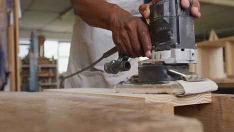 Mid-section-of-african-american-male-carpenter-using-an-electric-grinder-to-grind-wooden-plank