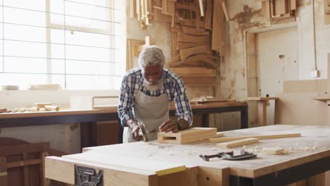 African-american-male-carpenter-hammering-nails-into-the-wood-at-a-carpentry-shop