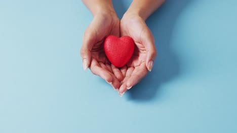 Vídeo-De-Manos-De-Mujer-Caucásica-Sosteniendo-El-Corazón-Sobre-Fondo-Azul