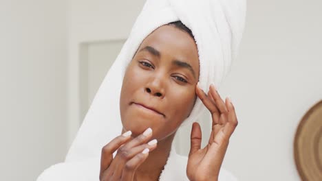 Video-Einer-Glücklichen-Afroamerikanischen-Frau-In-Robe,-Die-Ihr-Gesicht-Mit-Feuchtigkeit-Versorgt