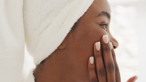 Video-of-happy-african-american-woman-in-robe-moisturizing-face