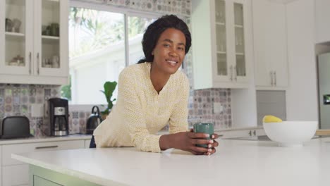 Video-of-happy-african-american-woman-drinking-coffee-in-kitchen