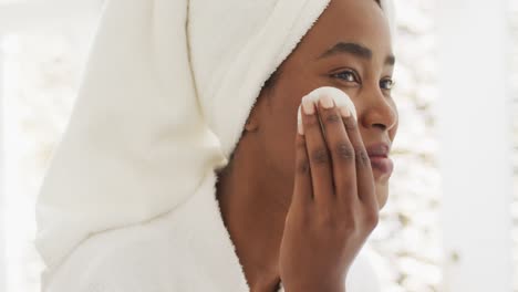 Video-Einer-Glücklichen-Afroamerikanischen-Frau-In-Robe,-Die-Ihr-Gesicht-Reinigt