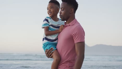Glücklicher-Afroamerikanischer-Vater,-Der-Seinen-Sohn-Am-Sonnigen-Strand-Trägt