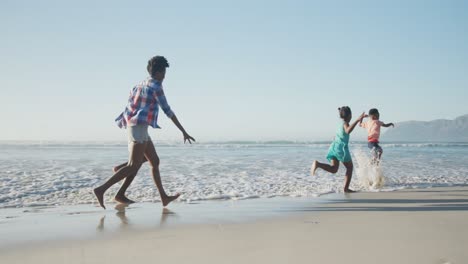 Happy-african-american-couple-running-with-daughter-and-son-on-sunny-beach