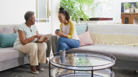African-american-daughter-with-coffee-cup-showing-her-mother-how-to-use-digital-tablet-at-home