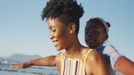 Glückliche-Afroamerikanische-Mutter,-Die-Ihre-Tochter-Am-Sonnigen-Strand-Trägt