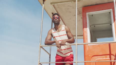 African-american-male-lifeguard-inspecting-on-tower-on-sunny-beach