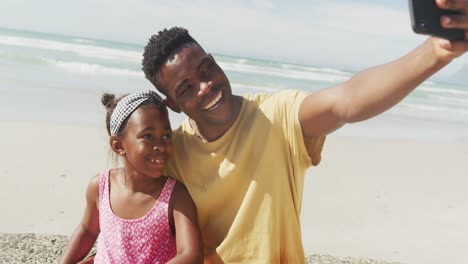 Afroamerikanischer-Vater-Und-Tochter-Unterhalten-Sich-Am-Strand-über-Ein-Selfie