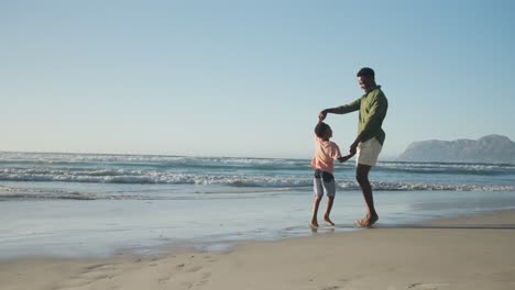 Glücklicher-Afroamerikanischer-Vater-Tanzt-Mit-Sohn-Am-Sonnigen-Strand