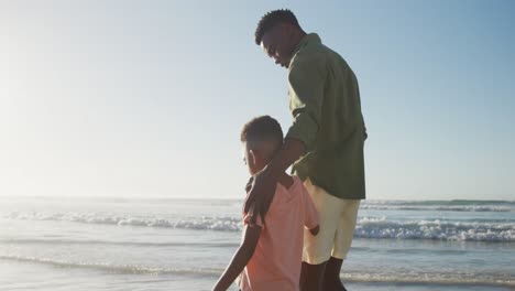 Glücklicher-Afroamerikanischer-Vater,-Der-Mit-Seinem-Sohn-Am-Sonnigen-Strand-Spaziert