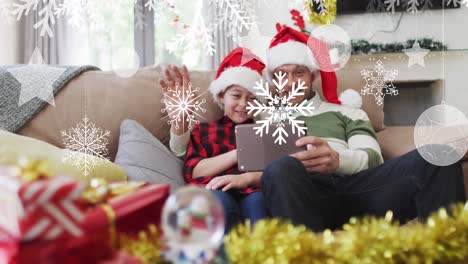 Animation-of-snow-falling-at-chrsitmas-over-happy-caucasian-father-with-son-having-video-call
