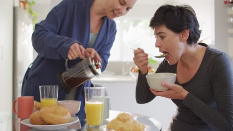 Kaukasische-Frau-Gießt-Kaffee-In-Eine-Tasse,-Während-Sie-Mit-Ihrer-Frau-Zu-Hause-Frühstückt