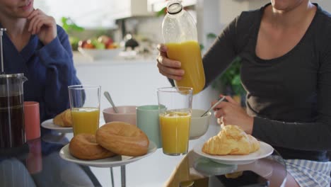 Caucasian-woman-pouring-juice-in-a-glass-while-having-breakfast-with-her-wife-at-home