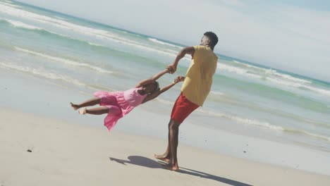 Verspielter-Afroamerikanischer-Vater-Dreht-Seine-Tochter-Am-Strand