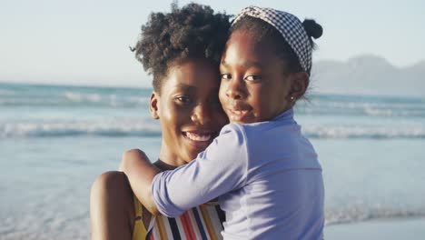 Porträt-Einer-Glücklichen-Afroamerikanischen-Mutter,-Die-Ihre-Tochter-Am-Sonnigen-Strand-Umarmt