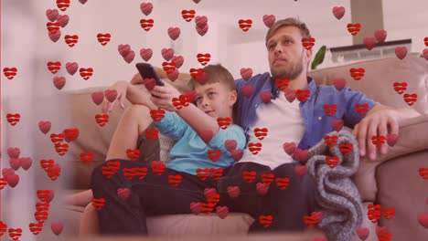 Animation-of-heart-icons-over-happy-caucasian-father-with-son-watching-tv