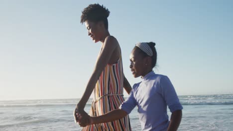 Glückliche-Afroamerikanische-Mutter,-Die-Mit-Ihrer-Tochter-Am-Sonnigen-Strand-Spaziert