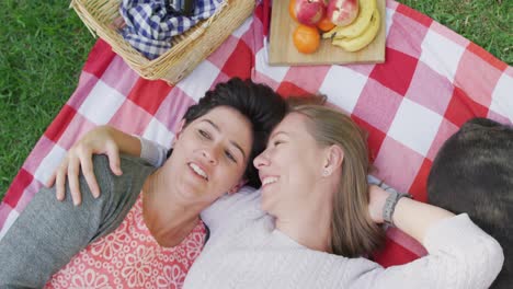 Overhead-view-of-caucasian-lesbian-couple-lying-on-the-blanket-in-the-garden-during-picnic