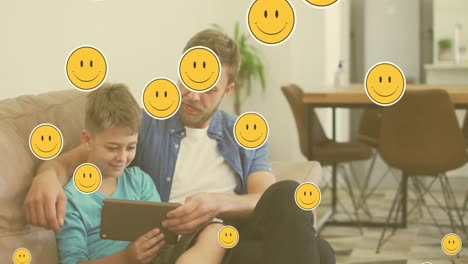 Animation-of-emoji-icons-over-happy-caucasian-father-and-son-using-tablet