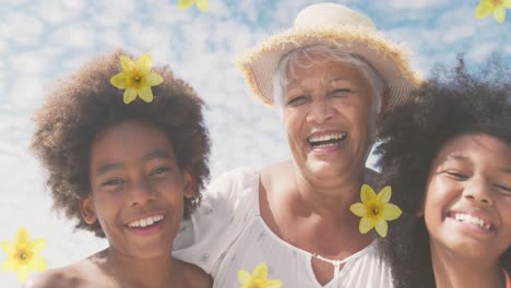 Animation-of-flowers-over-happy-senior-african-american-woman-with-grandchildren-on-sunny-beach