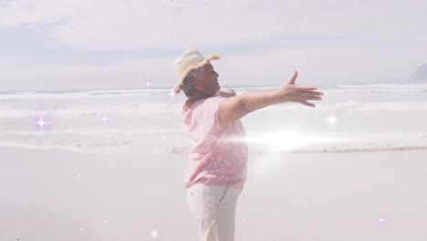 Animation-of-light-spots-over-happy-senior-african-american-woman-dancing-on-sunny-beach