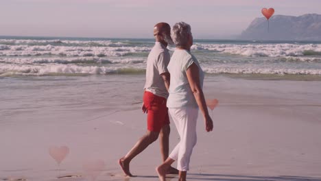 Animation-Von-Herzen-über-Einem-älteren-Afroamerikanischen-Paar,-Das-Am-Sonnigen-Strand-Spaziert