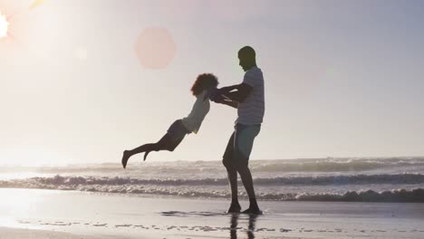 Animation-of-spots-over-happy-african-american-father-with-daughter-on-sunny-beach