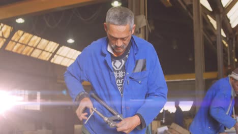 Animation-of-glowing-light-over-biracial-male-mechanic-in-workshop