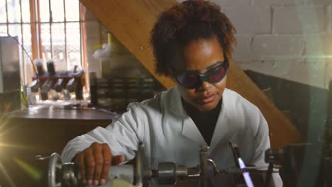 Animation-of-glowing-light-over-african-american-woman-working-in-workshop