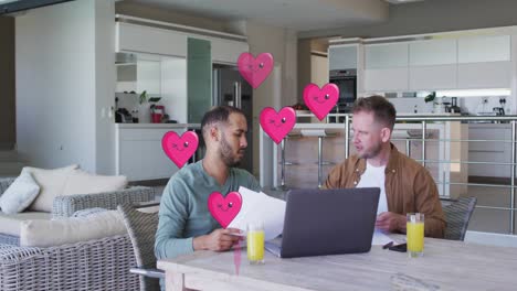 Animation-of-heart-icons-over-diverse-gay-couple-using-laptop