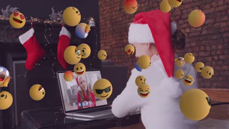 Animation-of-falling-emojis-over-women-wearing-santa-claus-hat-using-laptop