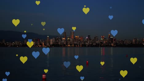 Animation-of-yellow-and-blue-hearts-floating-over-night-cityscape