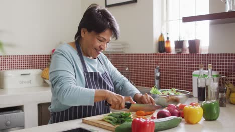 Asian-senior-woman-wearing-an-apron-chopping-vegetables-in-the-kitchen-at-home