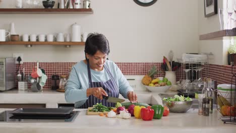Asiatische-Seniorin-Trägt-Eine-Schürze-Und-Hackt-Gemüse-In-Der-Heimischen-Küche