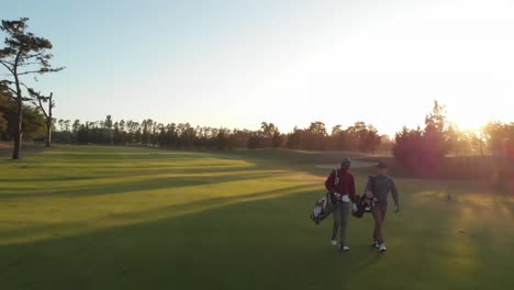 Two-diverse-male-golf-players-walking-at-golf-course-on-sunny-day