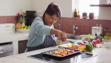 Mid-section-of-asian-senior-woman-preparing-vegetable-salad-in-the-kitchen-at-home