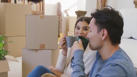 Video-of-happy-diverse-couple-drinking-coffee-in-new-house-after-moving-in