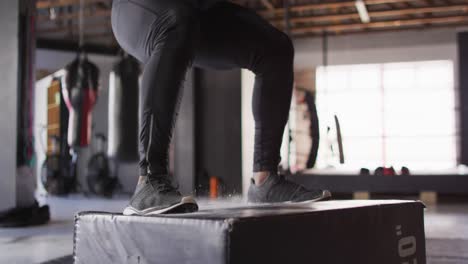 Video-Der-Beine-Eines-Fitten-Afroamerikanischen-Mannes,-Der-Im-Fitnessstudio-Auf-Einen-Block-Springt