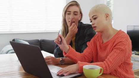 Happy-diverse-female-couple-talking-and-using-laptop-in-living-room